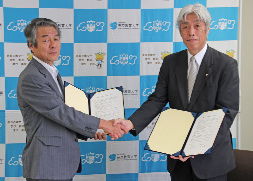 署名後に握手する長友学長（左）と生田教育長